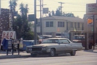 A cadillac de ville is parked on the side of a street next to a sign for BBQ