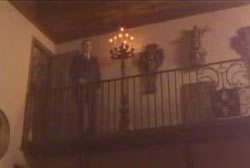 A man in a suit looking down from a balcony in a haunted house.