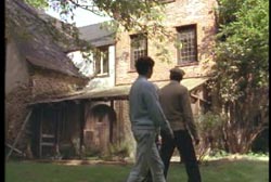 Two men looking at the back of the mansion as they walk through the yard. 