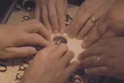 Six hands on the planchette on a oujia board.