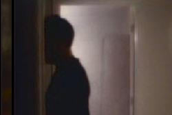 A man hidden in shadow is walking in the hallway outside the bedroom door.