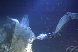 A mechnical arm of a submarine touches a submerged navy bomber.