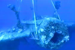A crane lifts a submerged navy bomber through the water.