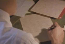 A man in a white shirt writing a letter.