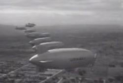 7 blimps flying in a line over a residential area.