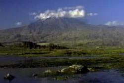 Mt. Ararat in Turkey. There is a large mountian, with clouds near the summit and a water in the forefront.
