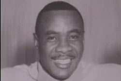 Sonny Liston smiling at the camera, wearing a white shirt.