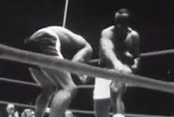 Sonny Liston is in a boxing ring, he is fighting Floyd Patterson who is double over after being punched in the face.