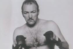 Chuck Wepner is holding his hands up in front of him wearing boxing gloves and no shirt.