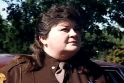 A woman with a brunette mullet, wearing a sheriff's deputy uniform.