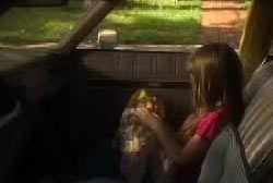 A young girl seats in the passenger seat of a station wagon, holding a toy.
