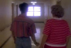 Two people walking down a white hallway, they are wearing red striped shirts.
