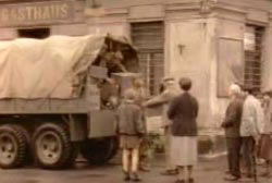 Several people are standing around a military truck as supplies are distributed during WWII.
