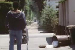 A man in a hoodie is standing with a grocery cart in an alley, there is trash can knocked over.