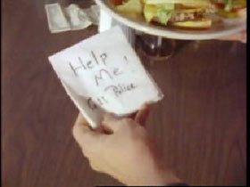 A female hand holding a note over a plate of fried in the dinner. The note reads 'Help me. 911 Police'