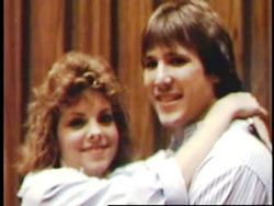 A man and woman, both with brown mullets and white shirts, hugging. 