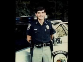Curtis Pishon posing in his police uniform infront of his patrol car.