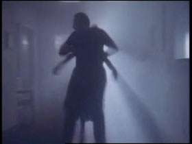 A man is dragging a woman down a hallway, both of them are in shadows.