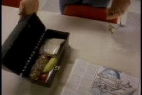 An open lunch box, a ring of keys and a newspaper are laid out on a table.