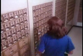 A woman in a blue shirt walking past rows of PO boxes.