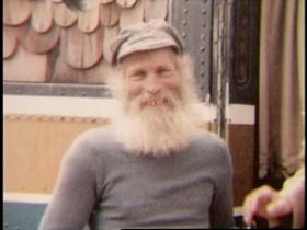 A elderly man, Hugh Harlin, with a white hair and beard wearing a grey sweater and cap.