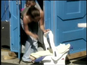 A woman leaves her baby carrier outside as she takes her toddler into a portapotty.