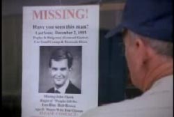 A man in a blue baseball cap looks at a missing poster for John Cheek.