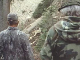 Two men in camo walking down a trail in the woods.