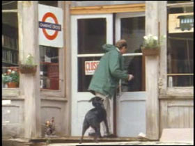 A man walking into a small shop with a black dog.