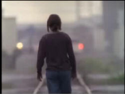 A person with short hair walking down train tracks.