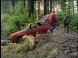 A red sedan is found by two people after being abandoned in a forest.