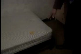A police officer points to a small yellow stain on a mattress.