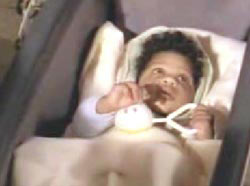 An african american baby in a crib holding a small baby rattle, Laurence Harding.