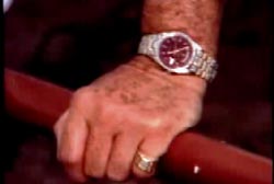 A hand with a ring on the pinky and a gold watch holding a red railing.