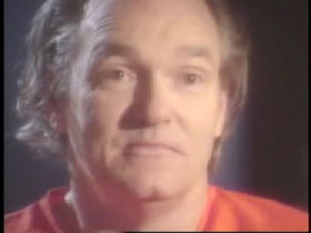 A caucasian middle aged man with shoulder length hair in an orange jumpsuit, Franklin Delano Floyd.