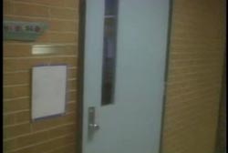 A school hallway, the wall has yellow tiles and the white door to the classroom has a small window.