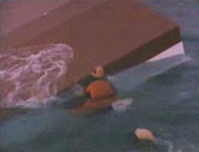 A man in an orange life vest holding onto the overturned hull of a ship.