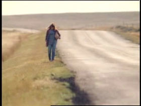 A woman with a bag over her shoulder walking down a remote road.