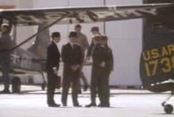 Four men in suits and hats standing near military aircrafts.
