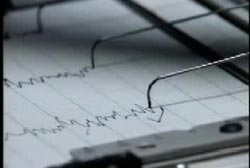 A close up image of a polygraph test. The needles are drawing the lines on the paper.
