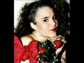 Star Palumbo wearing a off the shoulder red dress and holding three roses close to her face.