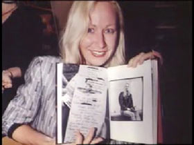 Susan Walsh posing holding open a book to show a piece of artwork she did.