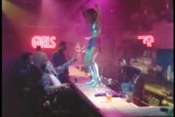 A dancer dancing on a bar in a strip club as several people look up at her.