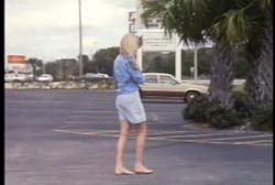 A woman without shoes walking through an empty parking lot.