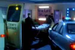Two coroners roll a gurney from their car into a building.