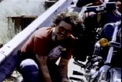 Tom Roche crouching down next to a motorcycle