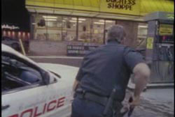 A police officer squats behind his police car outside the grocery store.
