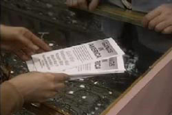 A person puts down flyers on a glass displaly case, the flyers says 'Gangs in America'. 