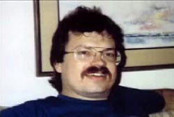A middle aged caucasian man, David Merrifield, with short brown hair, a mustache, and large wire rimmed glasses.