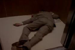 A man in a brown suit is laying face down in an elevator.